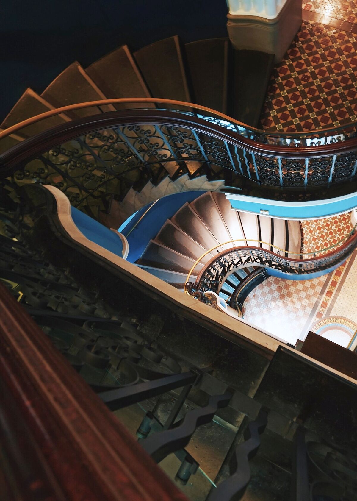 A cast-iron and mahogany staircase spiralling down past tessellated tiled landings, seen from above