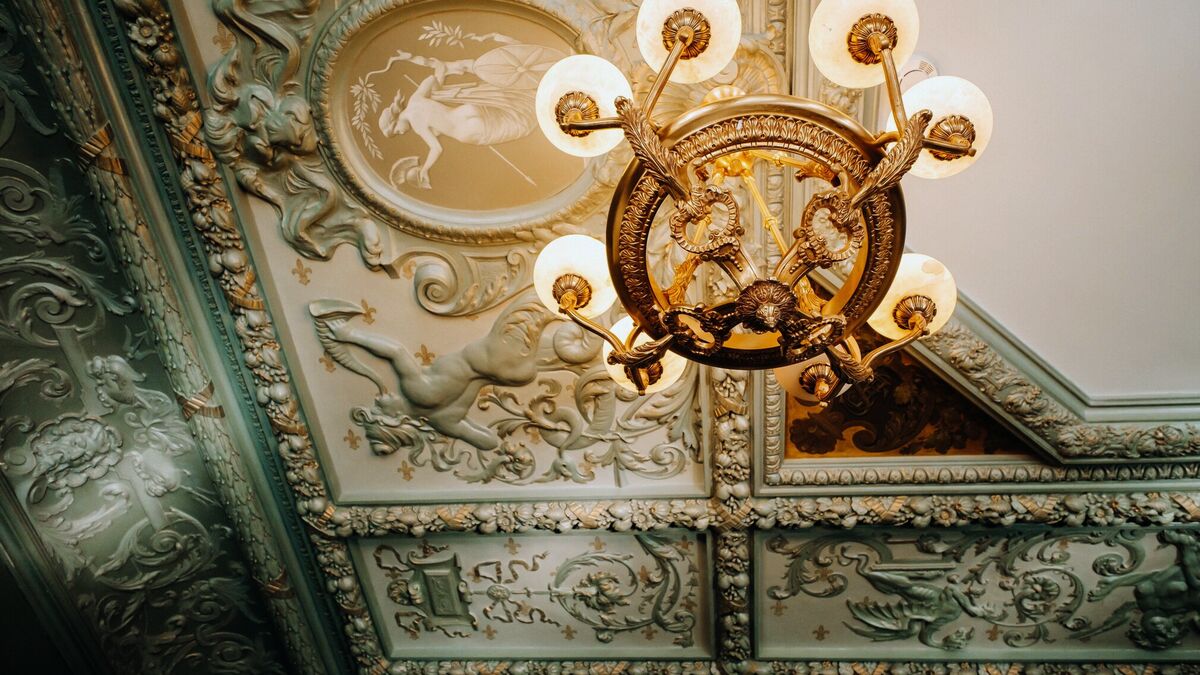A gilt-bronze chandelier hung from a palace ceiling of pale green plasterwork moulded with figures and scrolling foliage