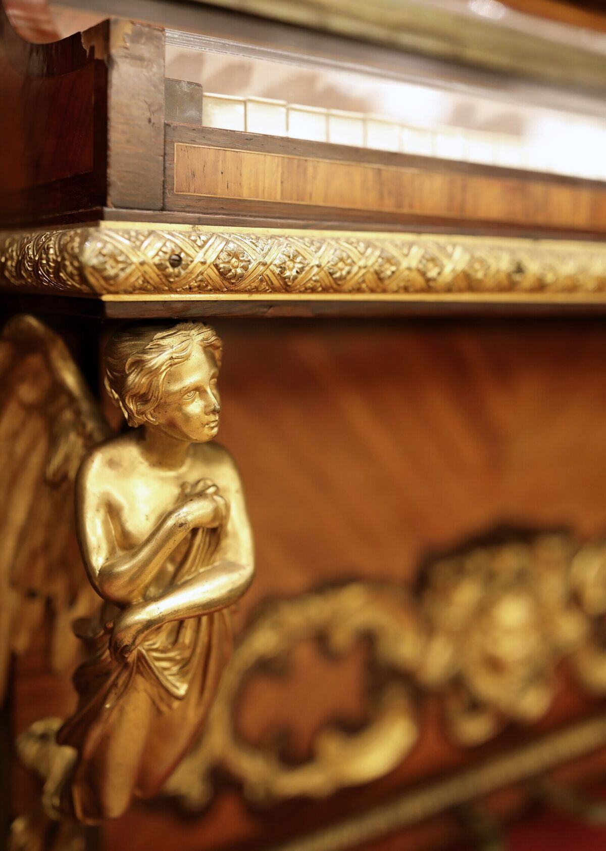 A gilt-bronze winged figure mounted at the corner of a marquetry cabinet, below a band of cast foliage