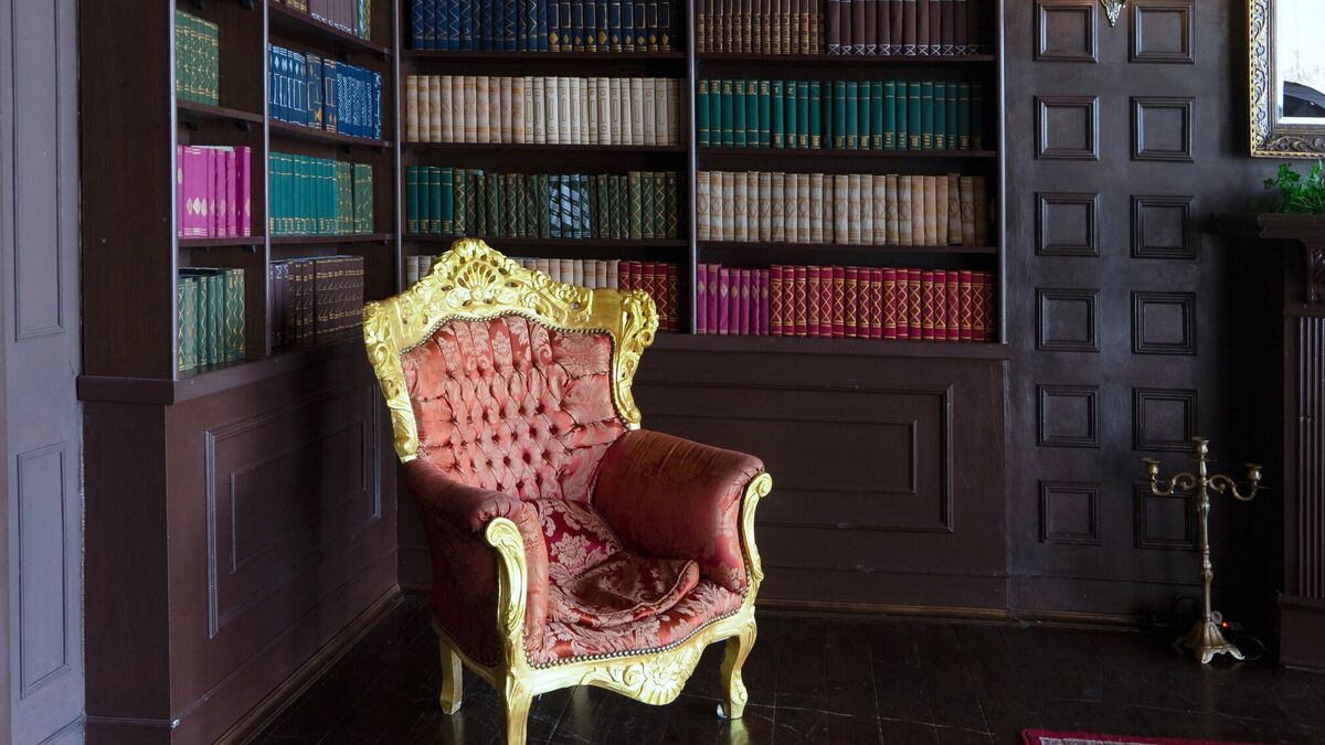 A giltwood armchair upholstered in red silk damask standing before the shelved books of a panelled library