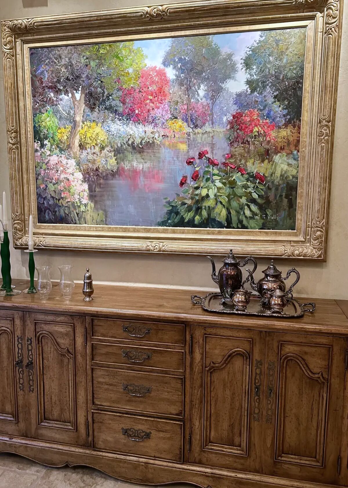A silver tea and coffee service on a salver, set on a carved sideboard beneath a gilt-framed impressionist garden painting