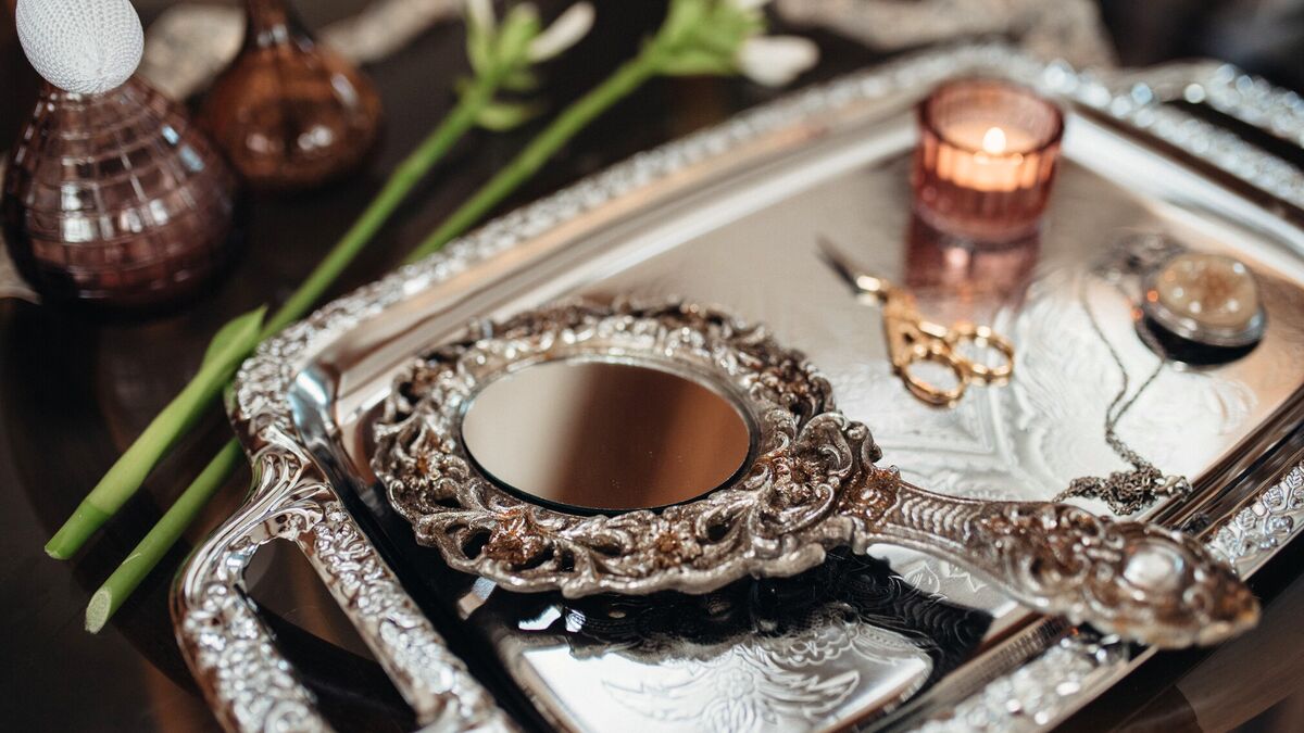 A silver dressing-table tray holding a repousse hand mirror, cut-glass scent bottles and a scatter of jewellery