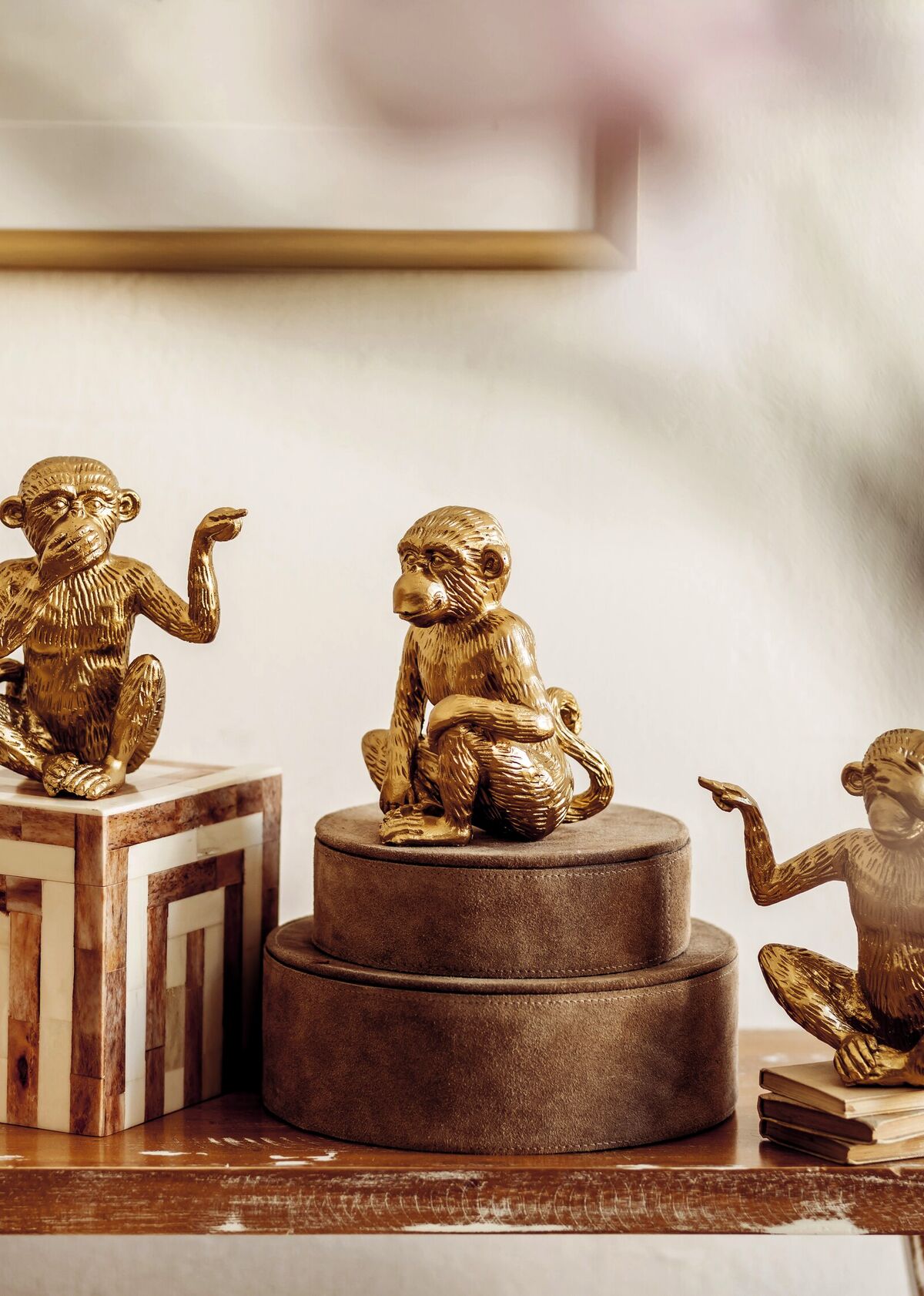 A row of gilt monkey figurines displayed on stacked lacquer boxes and books, staged on a console table