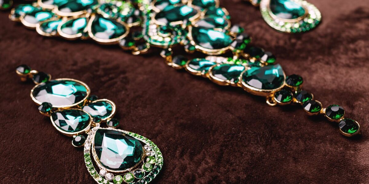 A gold necklace and matching drop earrings set with green gemstones, laid out on brown velvet