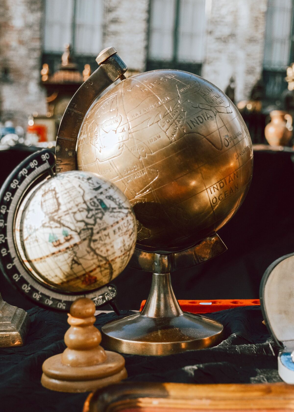 A table of collected objects — terrestrial globes, silver boxes, brass candlesticks and a Staffordshire spaniel set out together