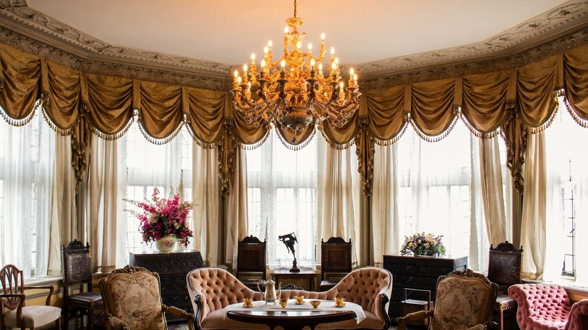 A bay-windowed parlor with silk swag valances, a gilt chandelier and Victorian parlor seating