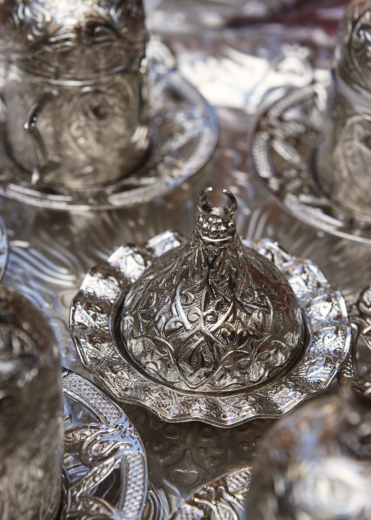 A set of chased silver coffee cups with domed lids and filigree saucers, closely grouped on a silver tray
