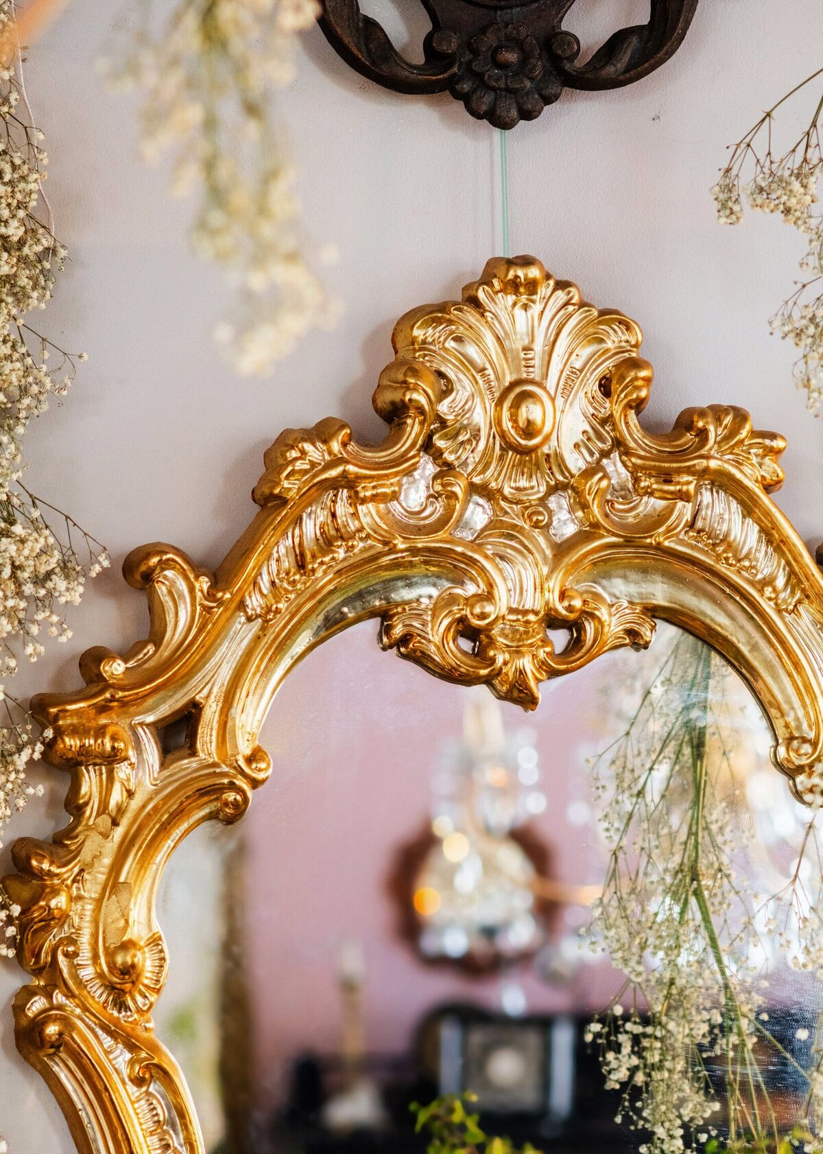 A carved giltwood rococo mirror hung beside a smaller shell-crested one, framed by trailing sprays of dried baby's breath