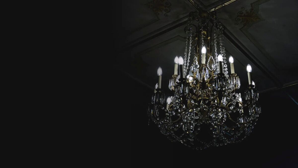 A crystal chandelier lit against a dark panelled ceiling