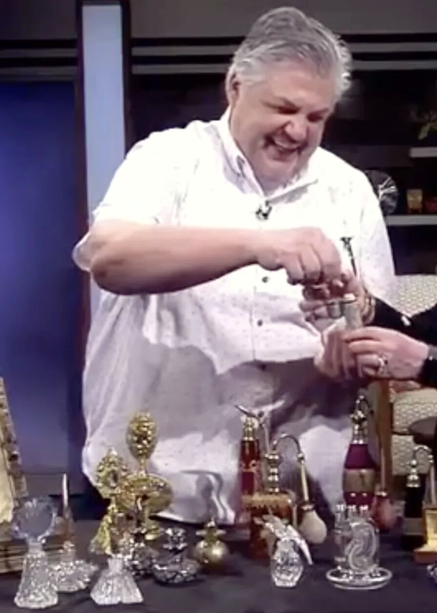 Gary Germer on the AM Northwest set, laughing as he hands an antique perfume bottle to the host across a table of cut-glass scent bottles