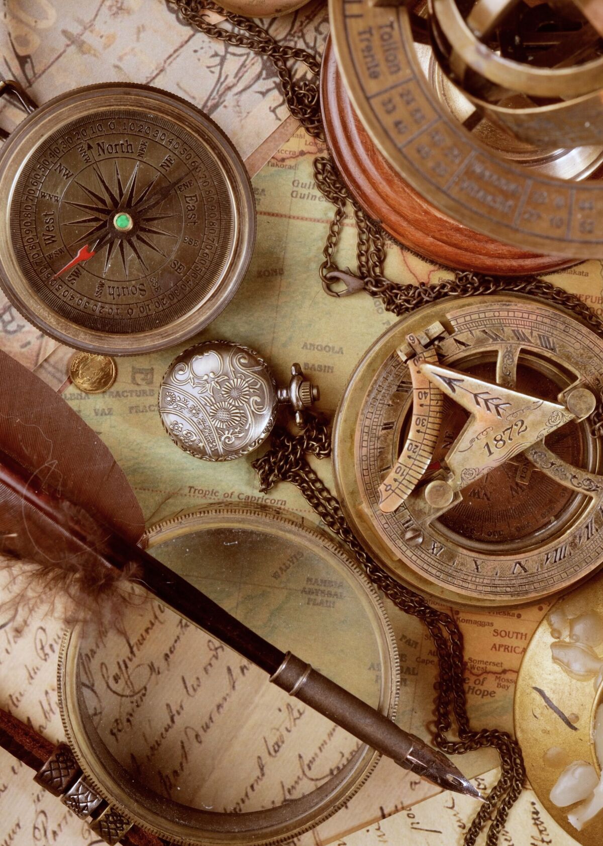 An antique map spread out with a quill pen, brass compasses and pocket instruments resting on top of it