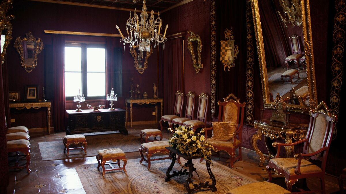 A red-walled period drawing room hung with gilt-framed mirrors and a chandelier above carved and gilded furniture